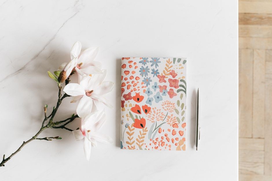 Floral notebook, pen and blossom arranged on a light table